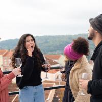 A group of diverse friends laughing and enjoying wine on a rooftop in Portugal.